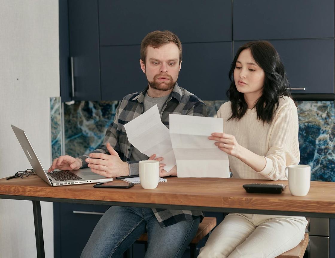 A couple reviewing paper bills and statements together at a kitchen table